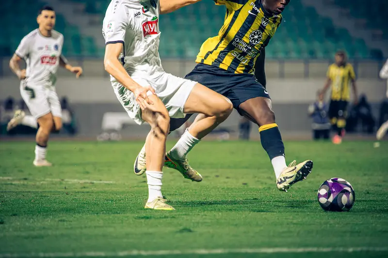 Footballers competing for the ball during a match in team kit